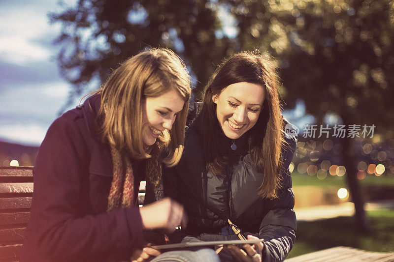 Two friends using digital tablet in the park, evening, fun